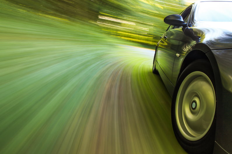 Side view of black sedan driving in forest.